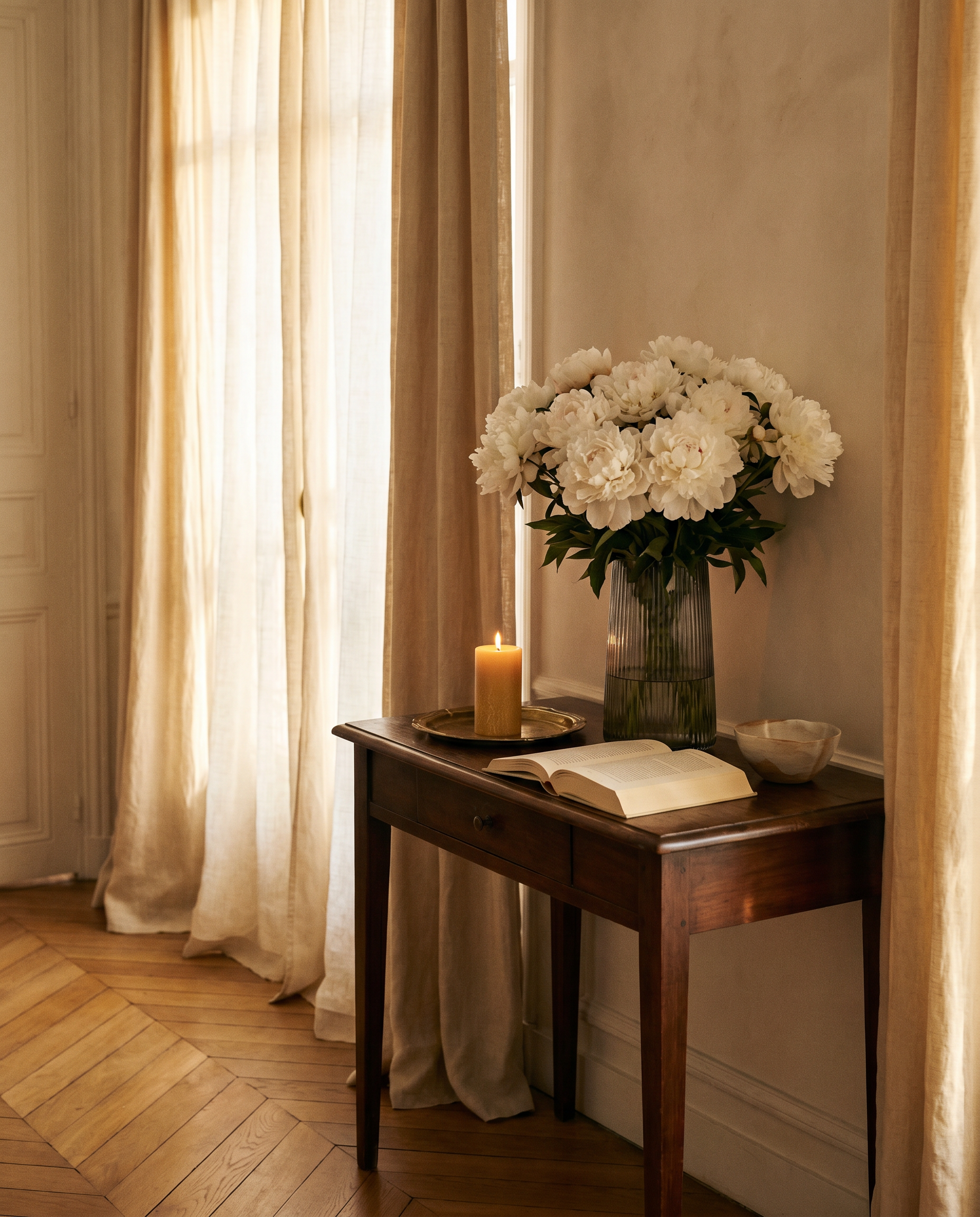 Parisian apartment interior at golden hour with peonies, a candle, and a book